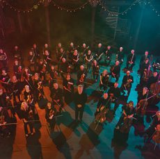 An image of the BBC SSO with Ryan Wigglesworth standing in a formation surrounded by coloured lights