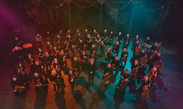 An image of the BBC SSO with Ryan Wigglesworth standing in a formation surrounded by coloured lights