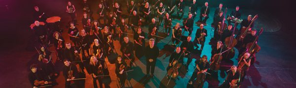 An image of the BBC SSO with Ryan Wigglesworth standing in a formation surrounded by coloured lights