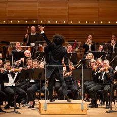 An image of a conductor and an orchestra performing on stage