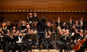 An image of a conductor and an orchestra performing on stage
