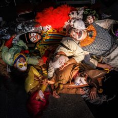 A group of people dressed as clowns laying in a heap on the floor
