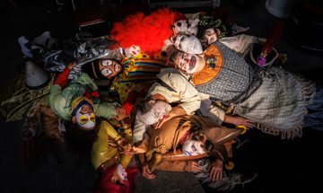 A group of people dressed as clowns laying in a heap on the floor