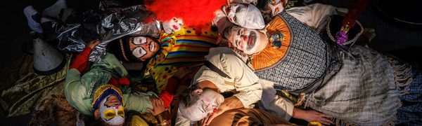 A group of people dressed as clowns laying in a heap on the floor