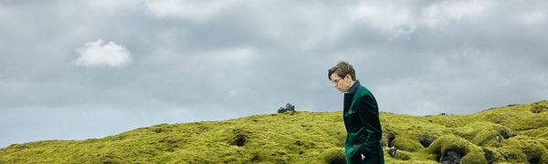 A man in a green jacket walking across a mossy hill