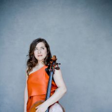 A woman wearing an orange dress resting her hands on a cello