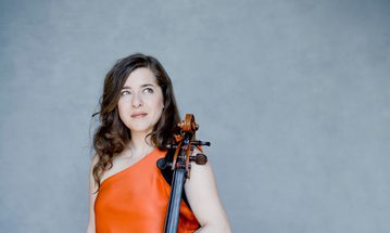 A woman wearing an orange dress resting her hands on a cello