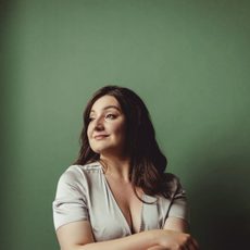 A woman wearing an off white dress smiling into the distance