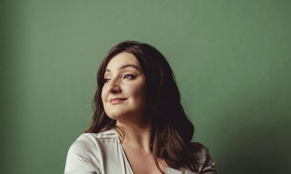 A woman wearing an off white dress smiling into the distance