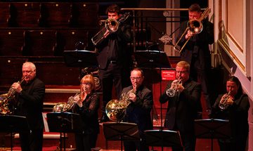 a group of brass musicians stand on stage