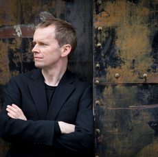 A man dressed in black leaning against a distressed looking door while looking off to the side