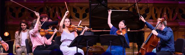 A group of string musicians on stage, holding their bows in the air