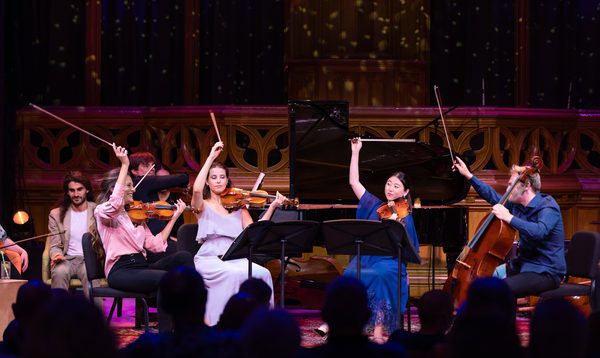 A group of string musicians on stage, holding their bows in the air