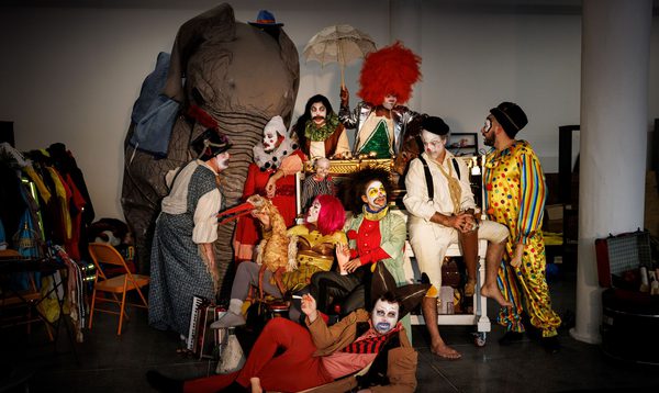 A group of people wearing clown costumes surrounded by circus props