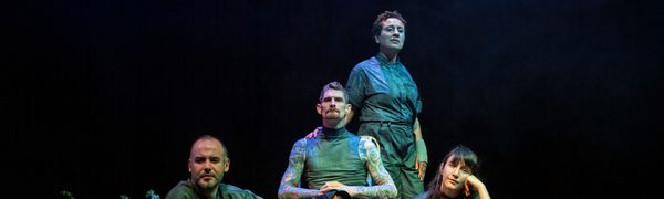 A group of performers sit on stage illuminated by a green light