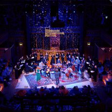 An ensemble of musicians performing on stage at The Hub surrounded by an audience