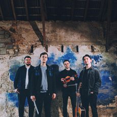 Four musicians standing in front of a distressed wall while holding their instruments