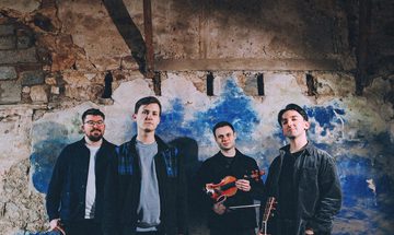 Four musicians standing in front of a distressed wall while holding their instruments