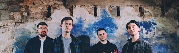 Four musicians standing in front of a distressed wall while holding their instruments