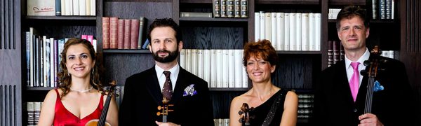 A quartet of musicians standing in front of a bookcase holding their instruments