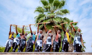 A group of women with vibrantly coloured hair stand in a row holding up drumsticks