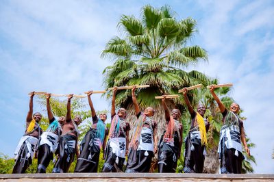 A group of women with vibrantly coloured hair stand in a row holding up drumsticks