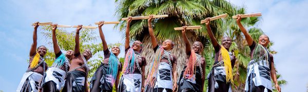 A group of women with vibrantly coloured hair stand in a row holding up drumsticks