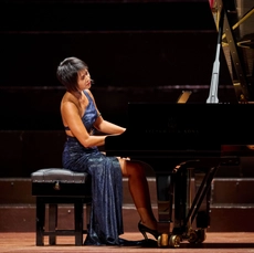 A woman wearing a blue dress playing a piano on stage