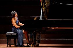 A woman wearing a blue dress playing a piano on stage