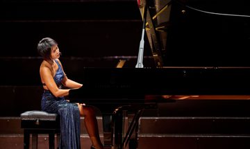 A woman wearing a blue dress playing a piano on stage