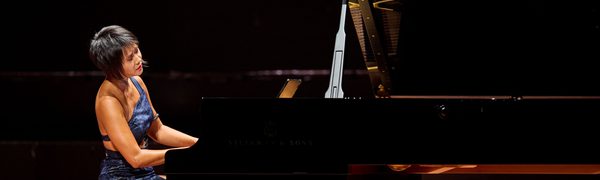 A woman wearing a blue dress playing a piano on stage