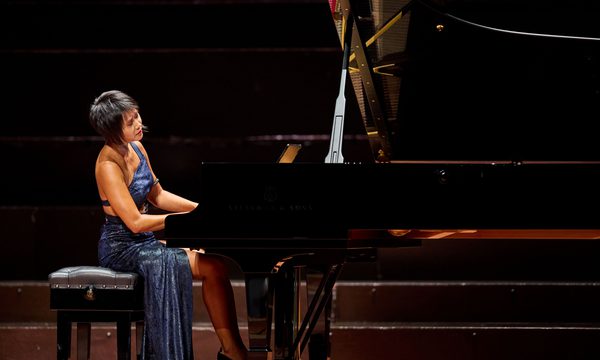 A woman wearing a blue dress playing a piano on stage