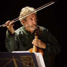 A man plays a viol, looking off to the right with his bow in the air
