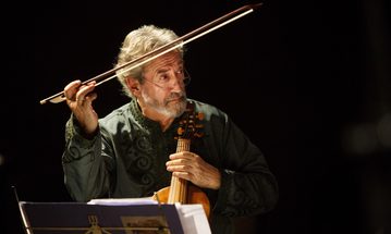 A man plays a viol, looking off to the right with his bow in the air