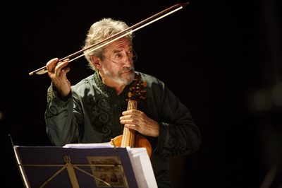 A man plays a viol, looking off to the right with his bow in the air