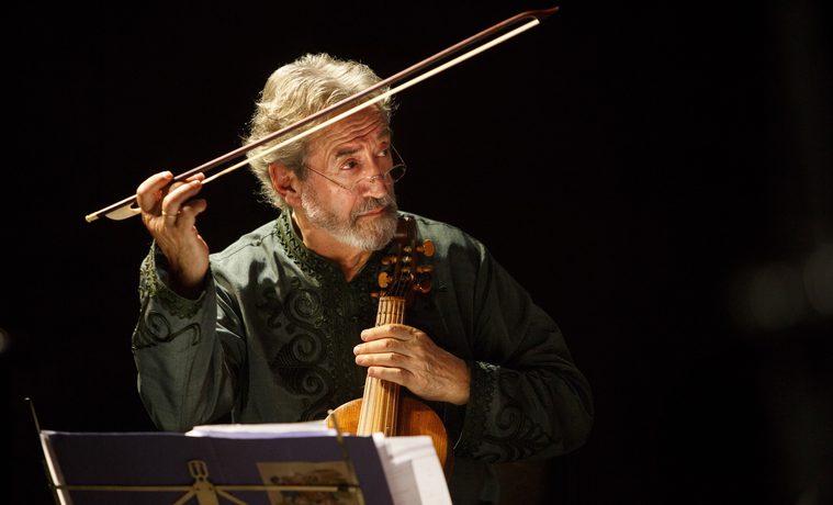 A man plays a viol, looking off to the right with his bow in the air