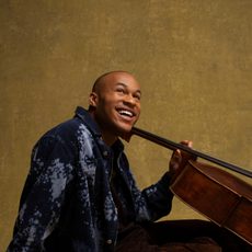 A man sitting on the ground holding a cello with a smile