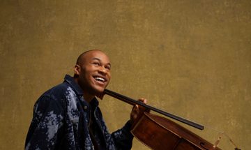 A man sitting on the ground holding a cello with a smile