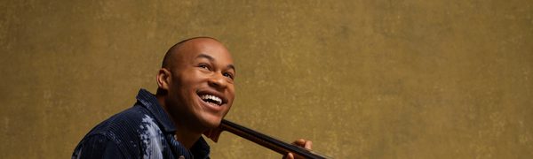 A man sitting on the ground holding a cello with a smile