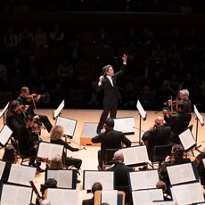 A conductor on stage facing the orchestra