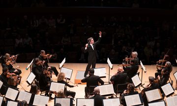 A conductor on stage facing the orchestra