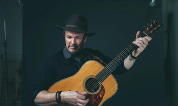 A man stands playing an acoustic guitar