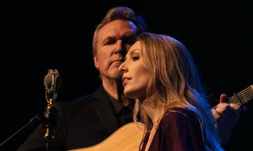 a women sings with a man playing guitar behind her