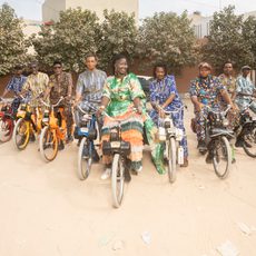 a group of people in colourful clothes sit on bikes smiling