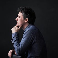 Side profile of a man with his chin resting in his hand looking off into the distance