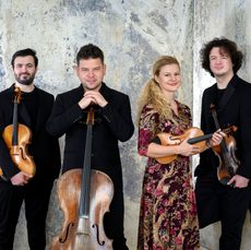 Four musicians stand holding their instruments and smiling at the camera