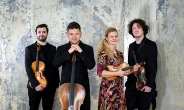 Four musicians stand holding their instruments and smiling at the camera