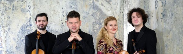 Four musicians stand holding their instruments and smiling at the camera