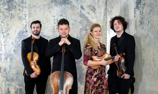 Four musicians stand holding their instruments and smiling at the camera