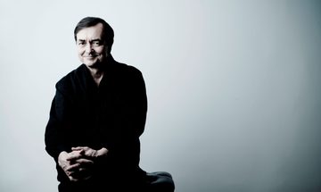 A man dressed in black sits in front of a white wall smiling at the camera